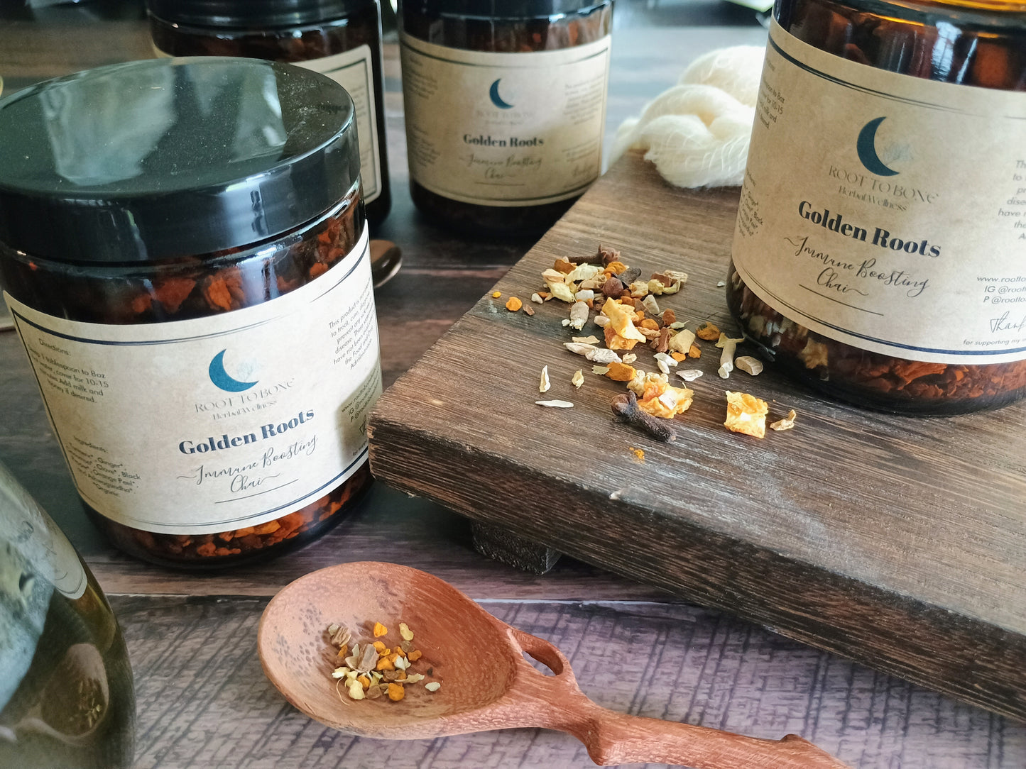 Jars of 'Golden Roots' on a wooden surface with a spoon containing dried herbs.