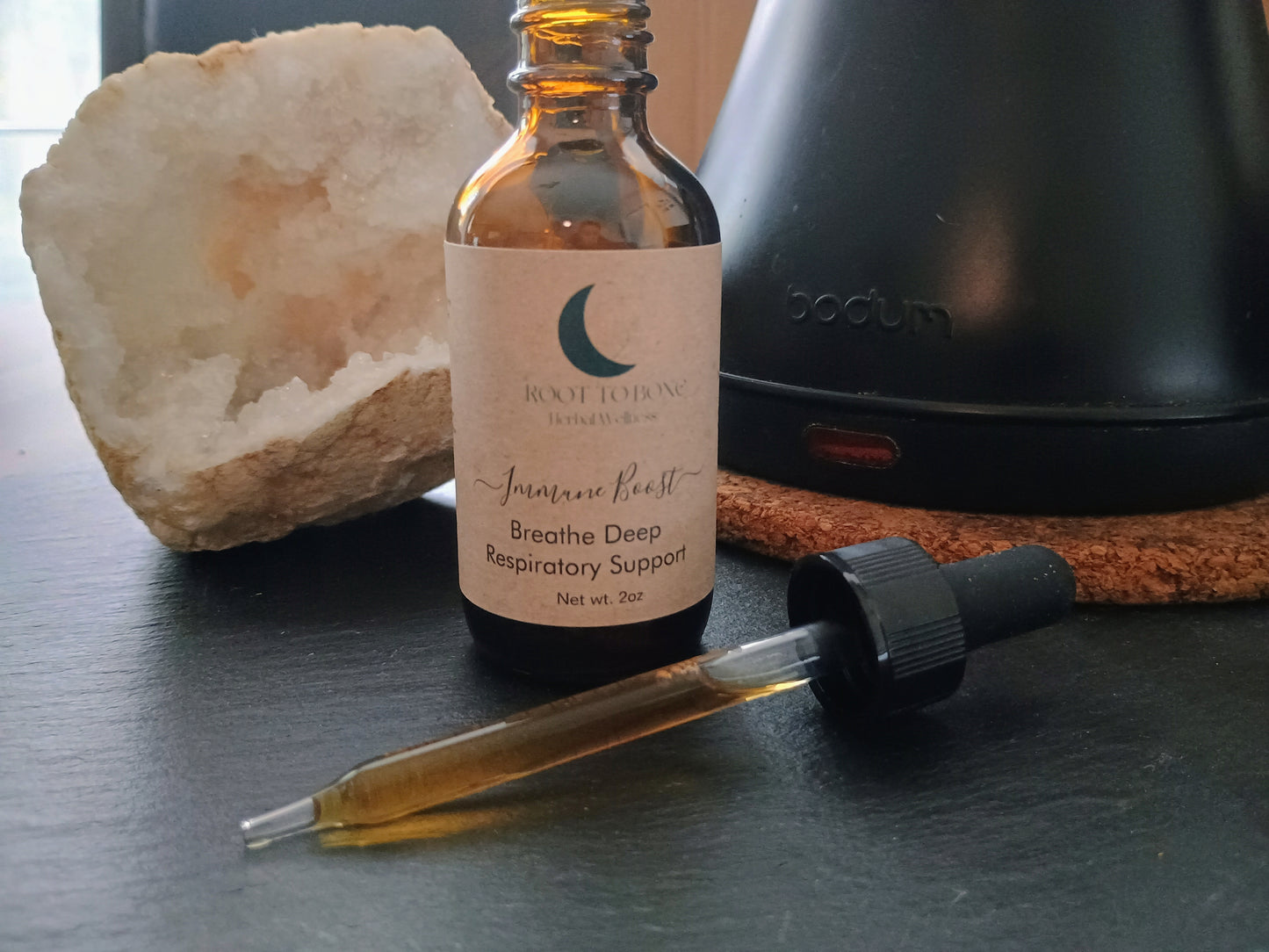 Bottle of respiratory support with dropper on a dark surface next to a crystal and teapot.