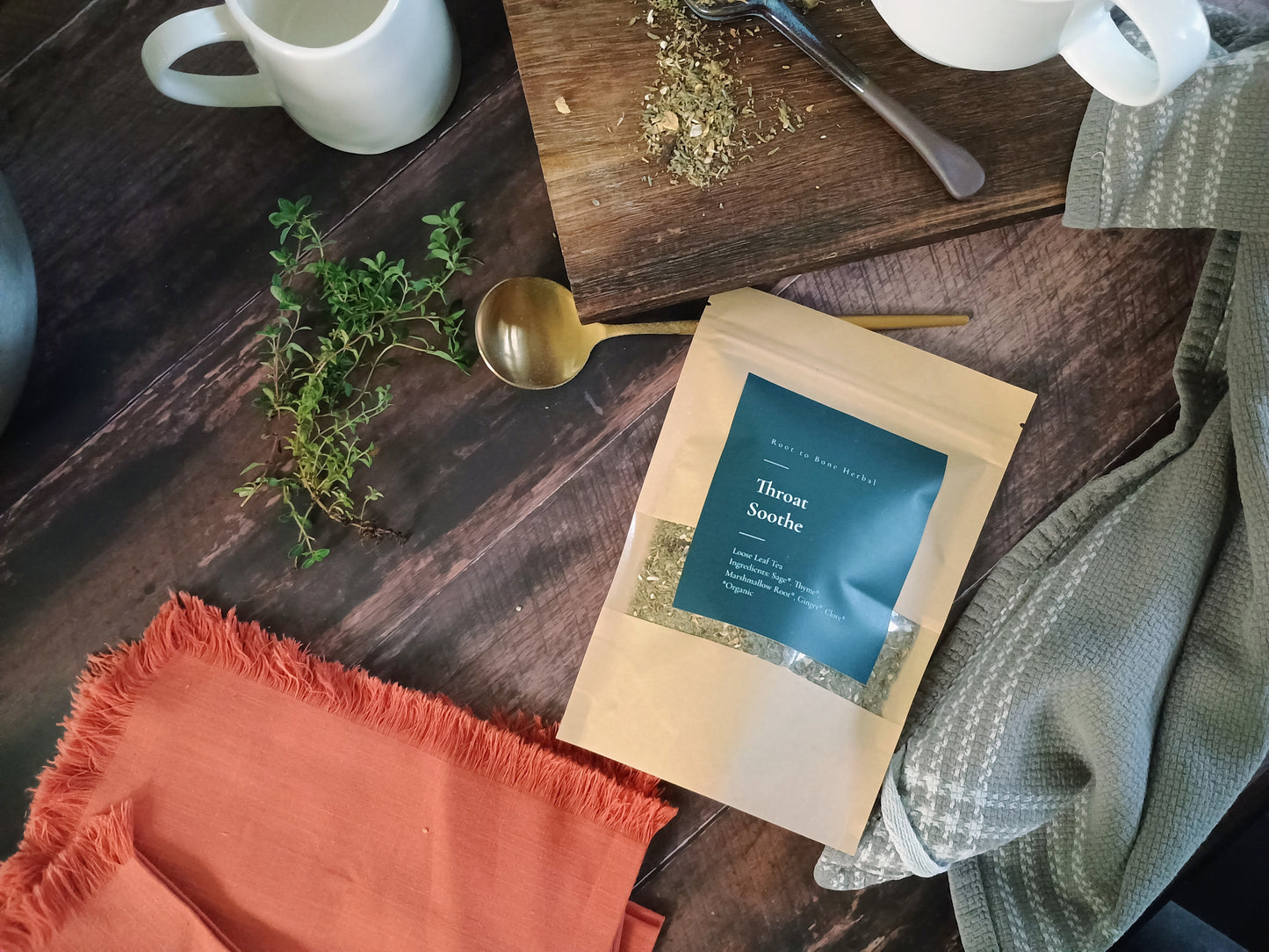 Tea package on a wooden surface with tea leaves and a spoon and thyme