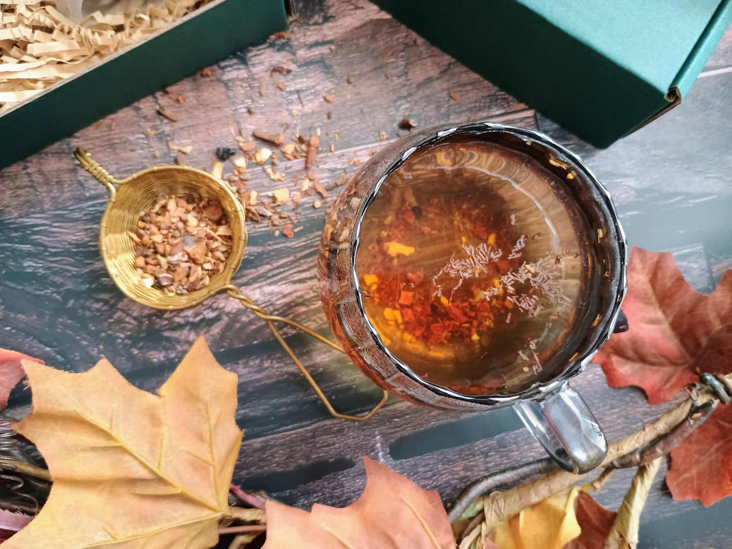 Tea cup with a decorative lid on a wooden surface with autumn leaves and a small sieve.