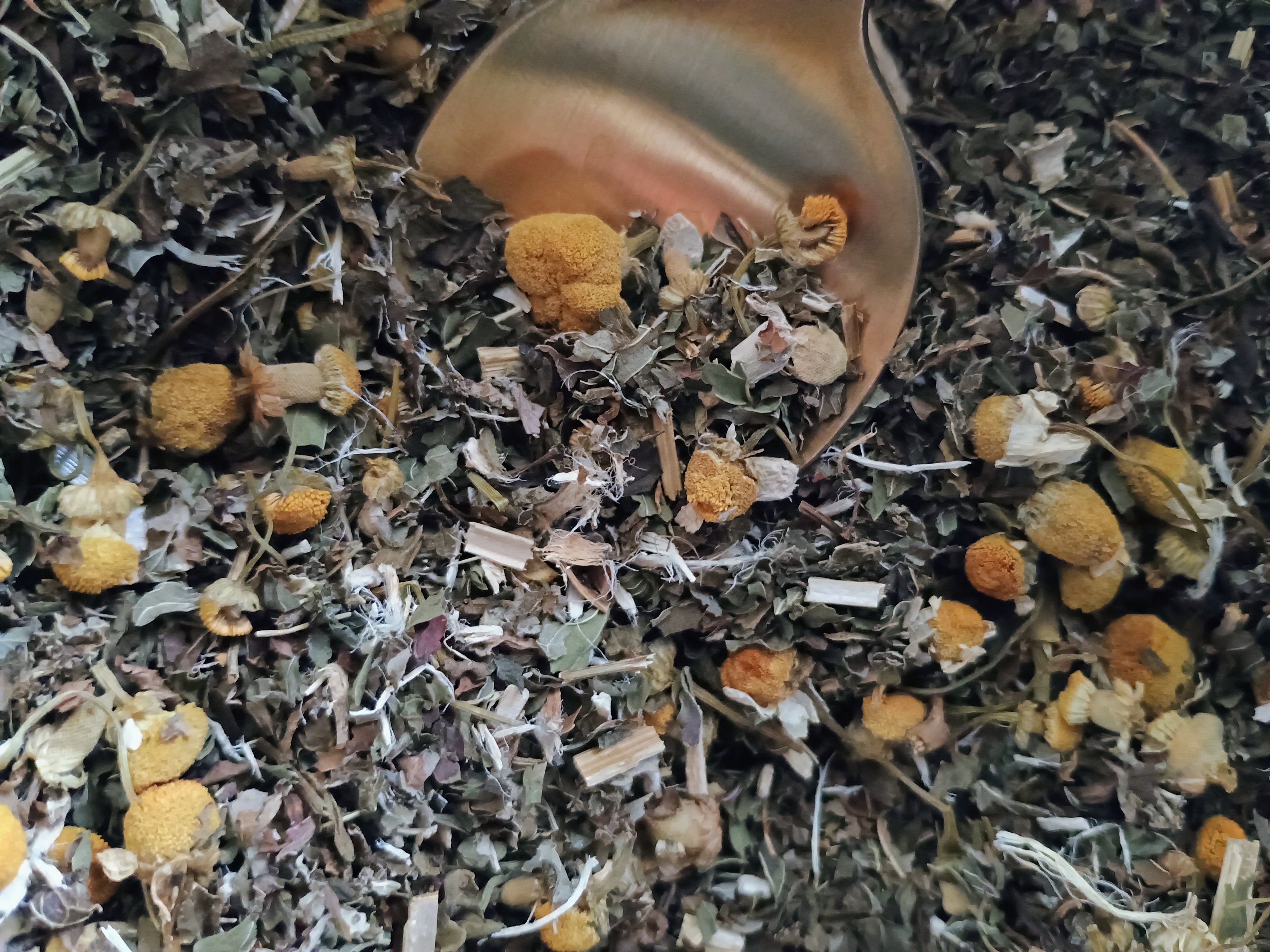 Close-up of dried herbs and flowers with a spoonful above