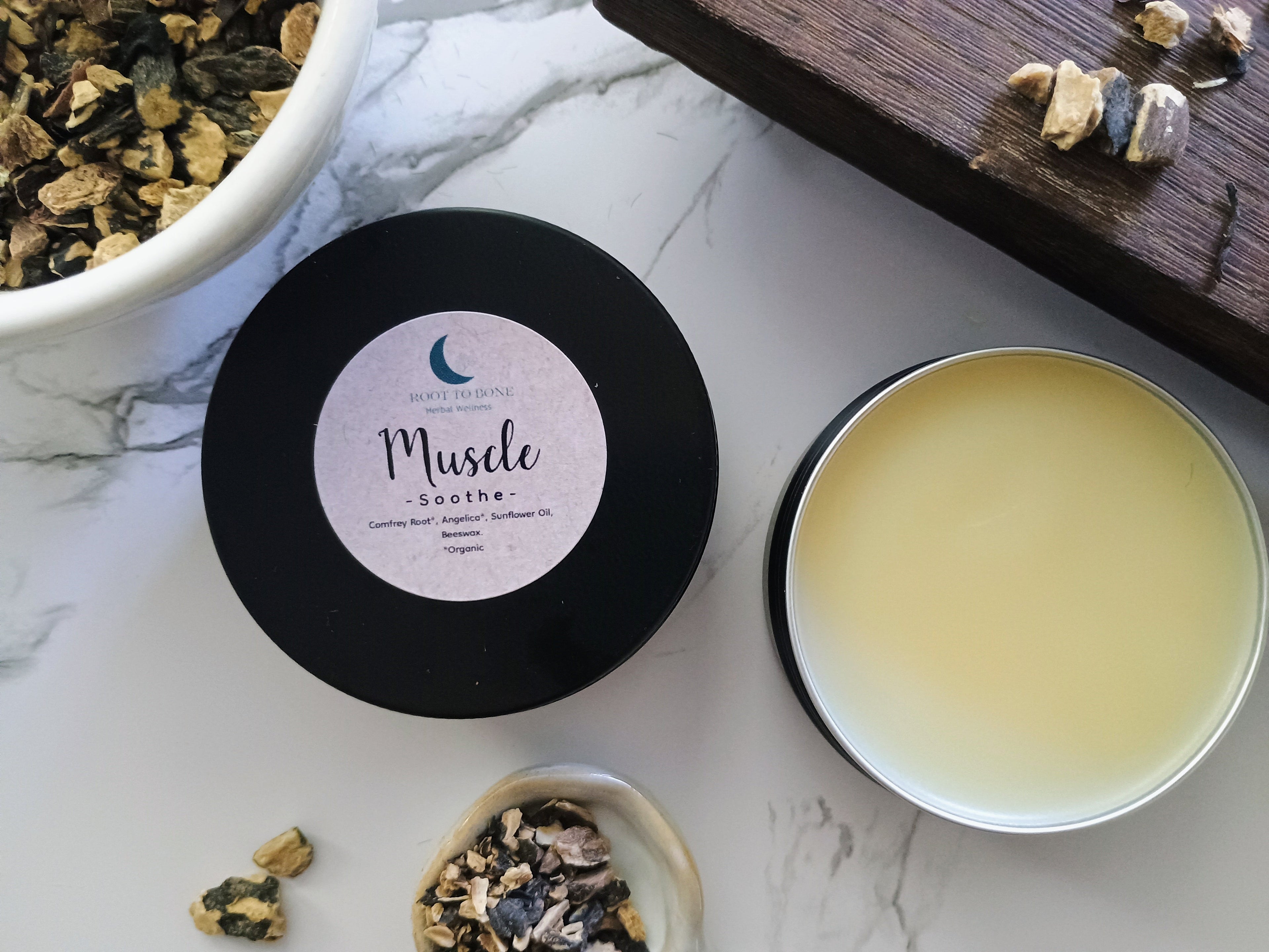 open tin of herbal salve next to comfrey root