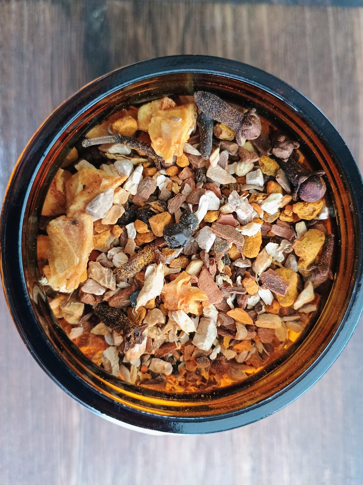 Top-down view of a container filled with various types of dried herbs on a wooden surface.