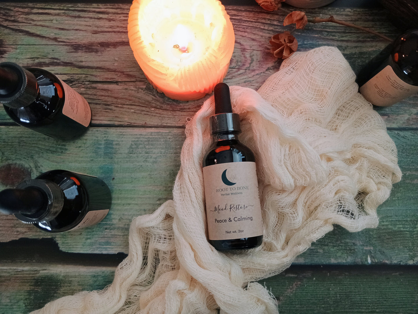 Bottle of 'Peace & Calming' tincture on a textured surface with candles and bottles in the background