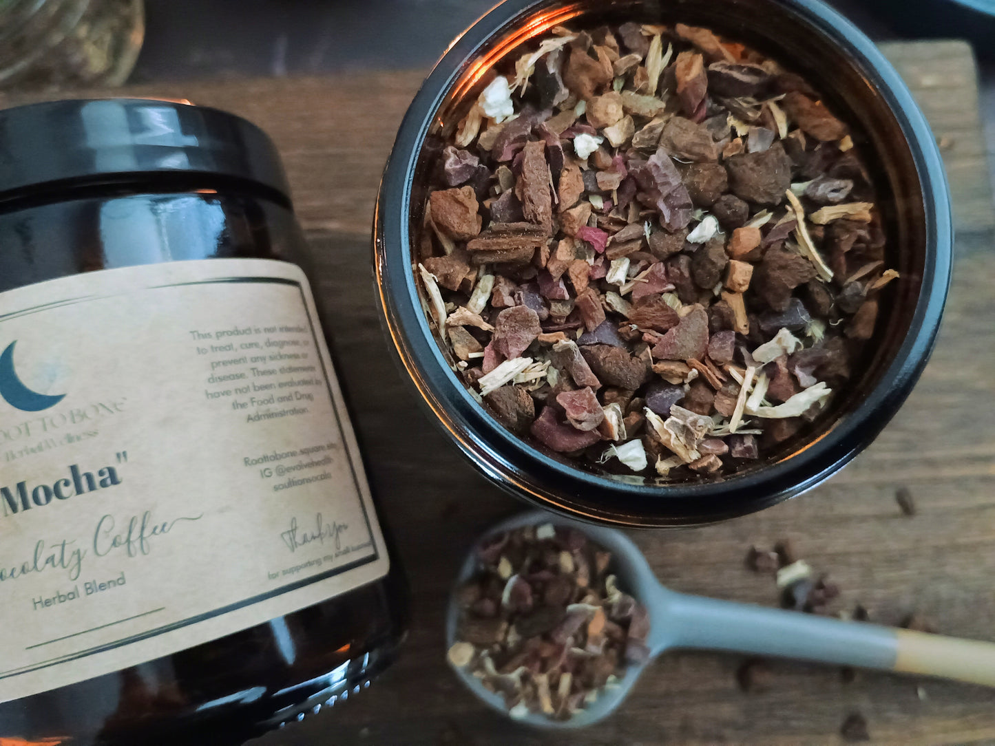Herbal blend in a black container with a bottle labeled 'Mocha' on a wooden surface.