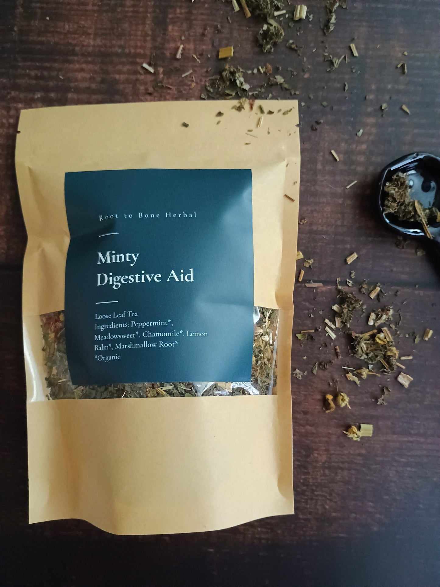Tea package labeled 'Miny Digestive Aid' on a wooden surface with loose tea leaves.
