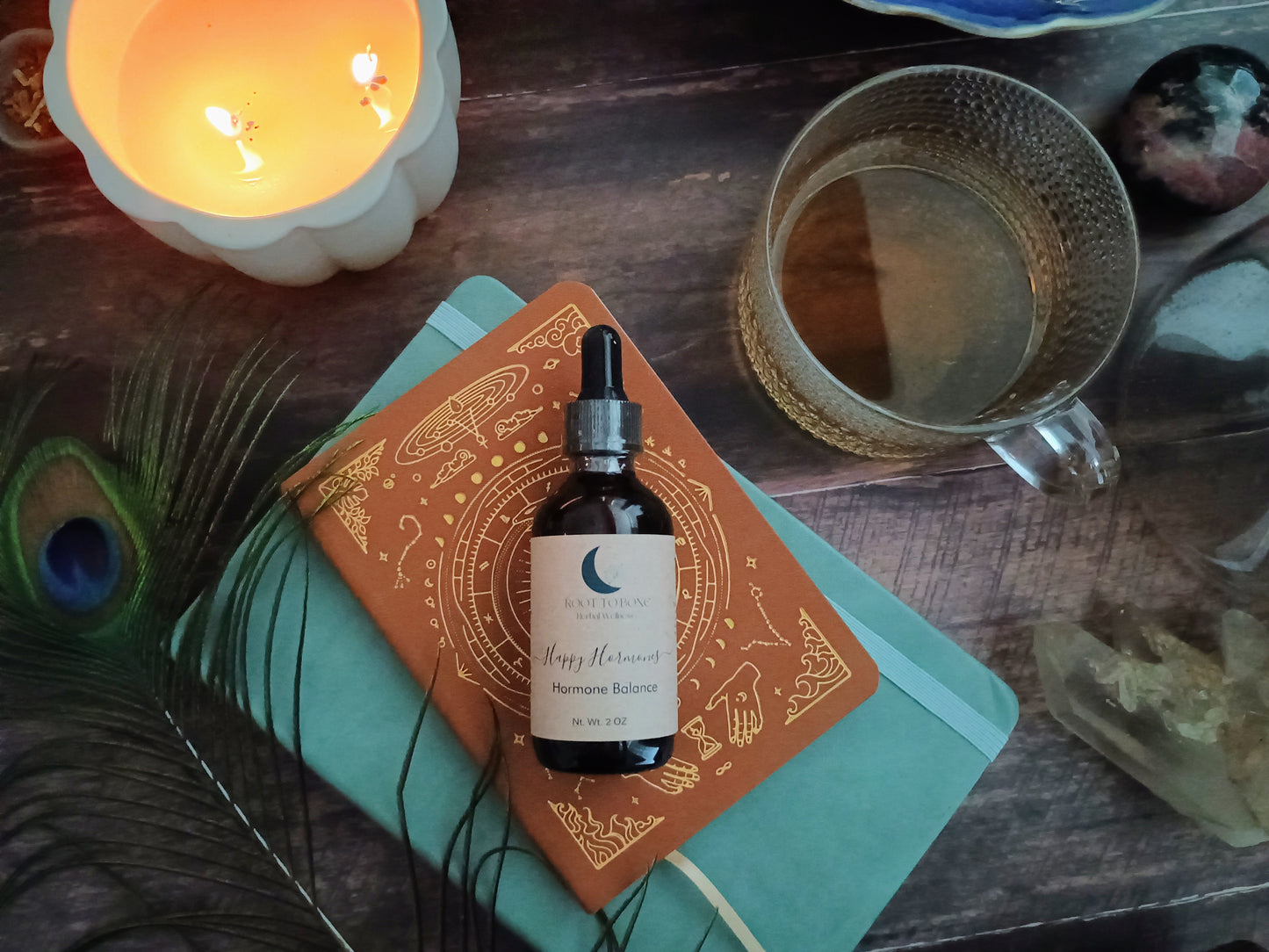 Bottle of 'Happy Hormones' hormonal balance supplement on an orange and gold book with a candle and teacup in the background.