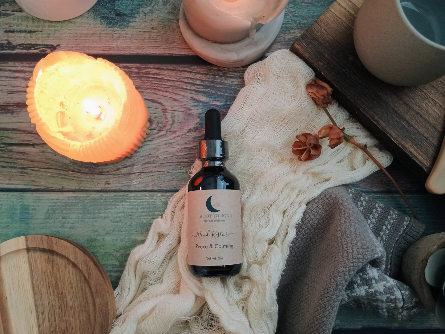 Bottle of 'Root to Bone Herbals' product on a textured surface with candles and wooden items.