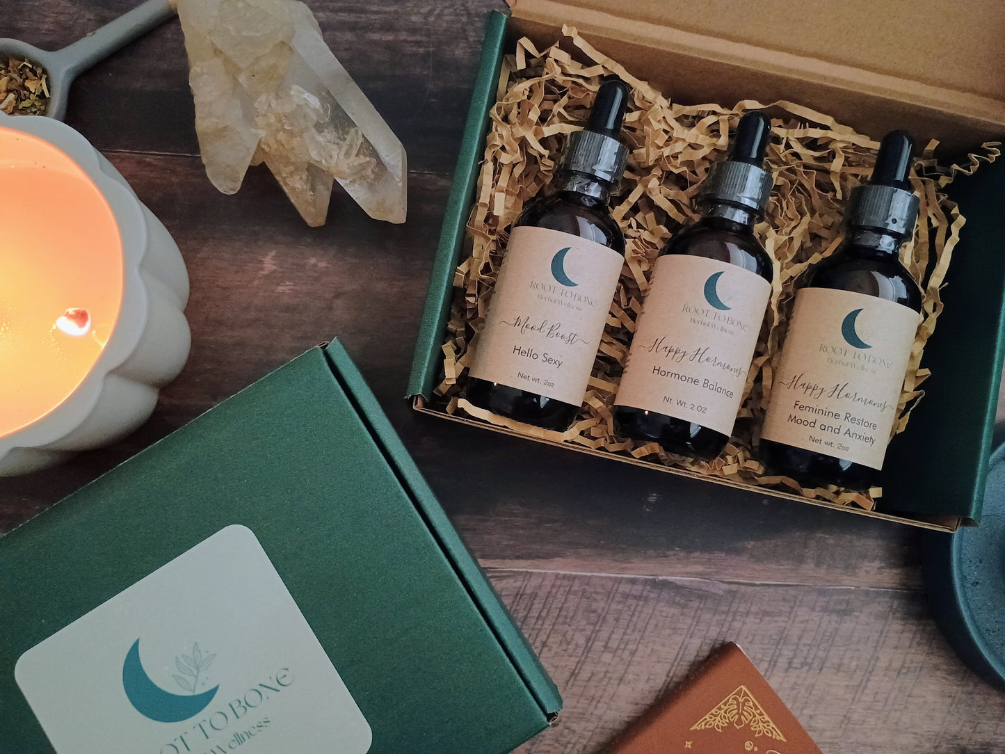 Three bottles of 'Happy Hormones' product in a gift box with a lit candle and decorative items on a wooden surface.