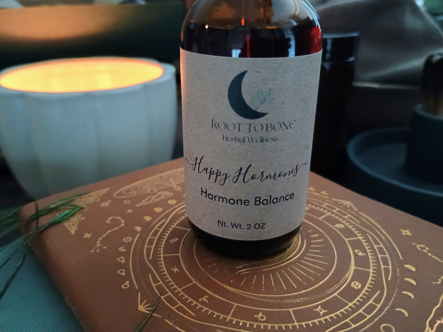 Bottle of 'Happy Hormones Hormone Balance' by Root to Bone on a decorative surface with a candle in the background.