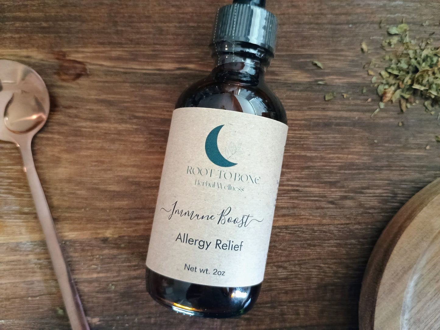 Bottle of Root to Bone Tinctures on a wooden surface with a spoon and dried herbs.