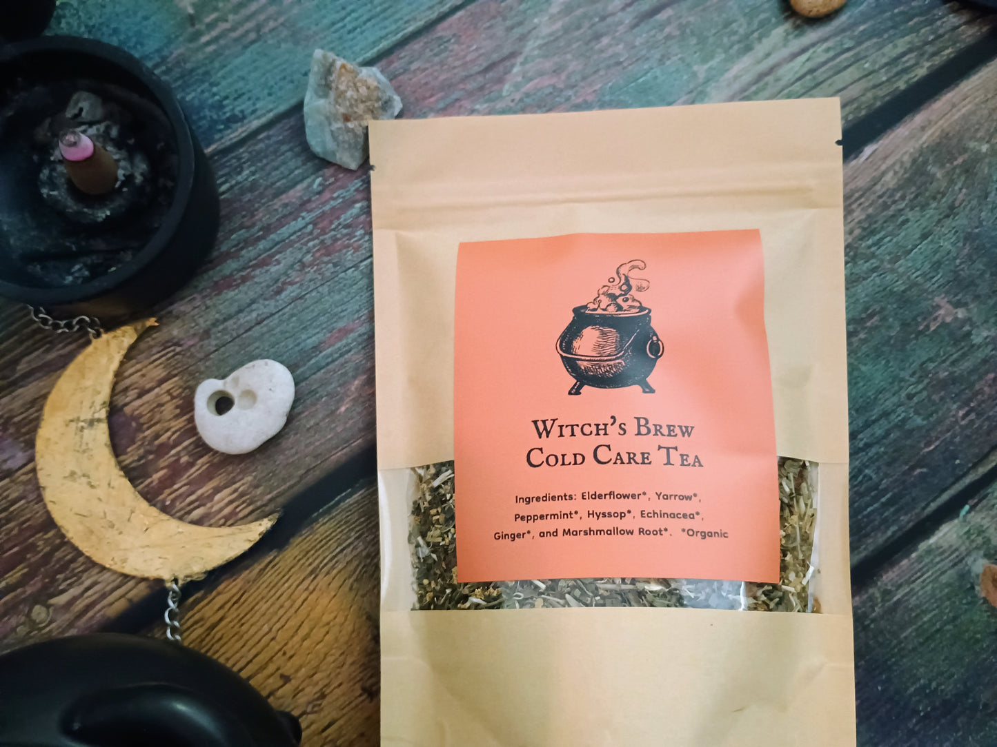 Witch's Brew Cold Care Tea package on a wooden surface with decorative items.