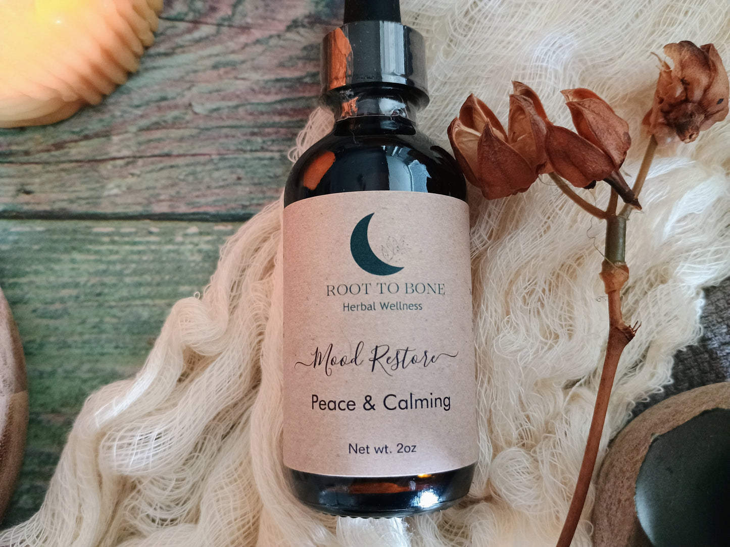 Bottle of 'Mood Restore' with 'Root to Bone' label on a textured surface with flowers.