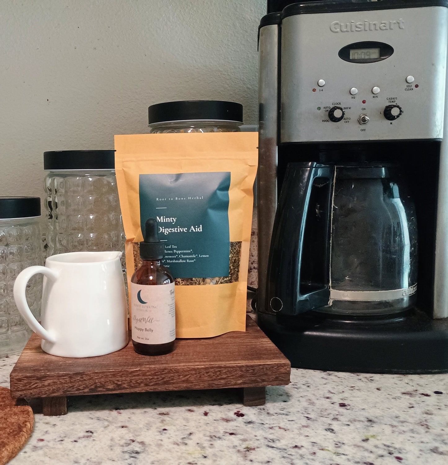 Cuisinart coffee maker with a mug, jar, and package of minty digestive aid on a wooden tray.