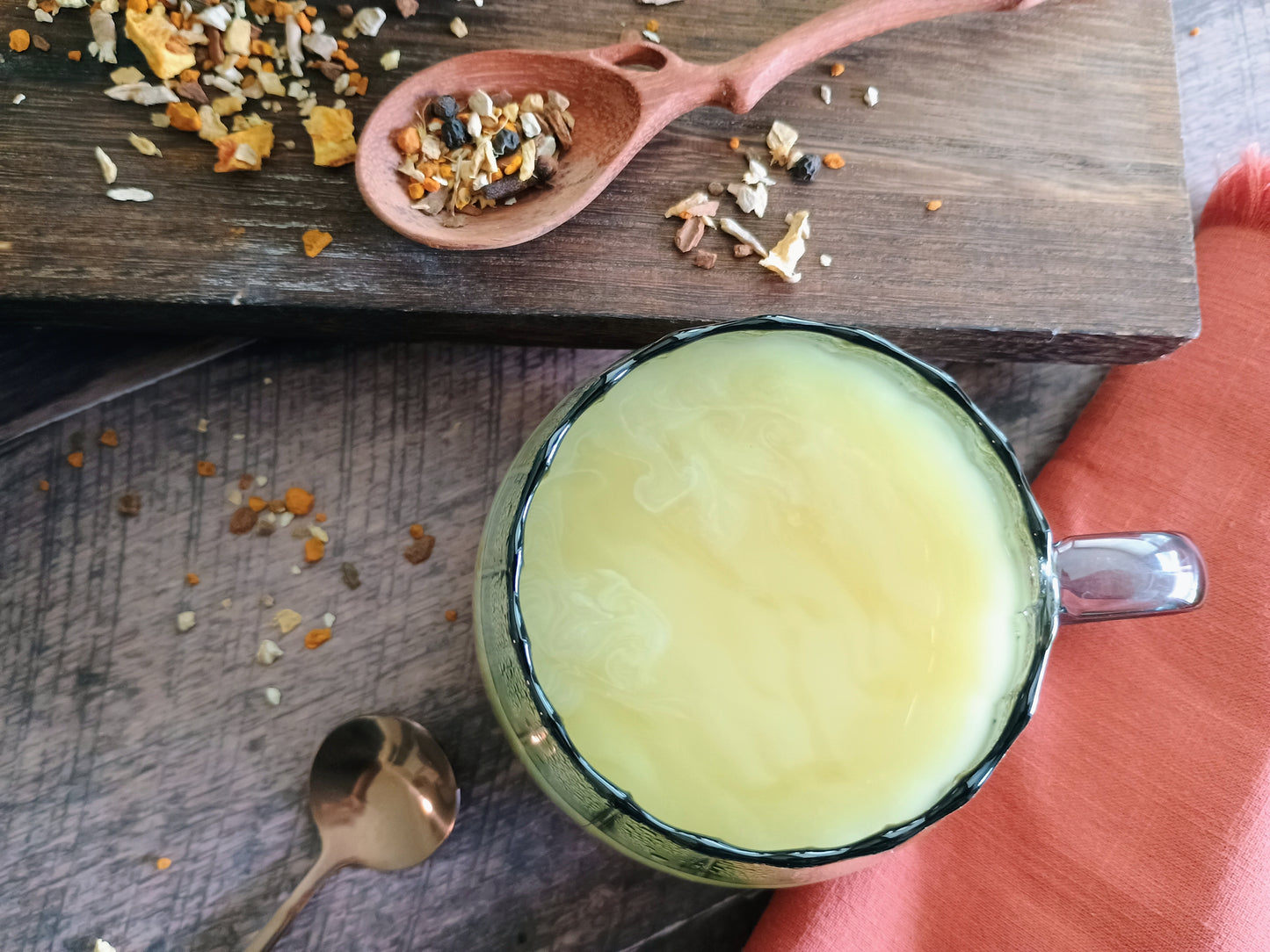 Tea cup with yellow liquid on a wooden surface with tea leaves and a spoon.
