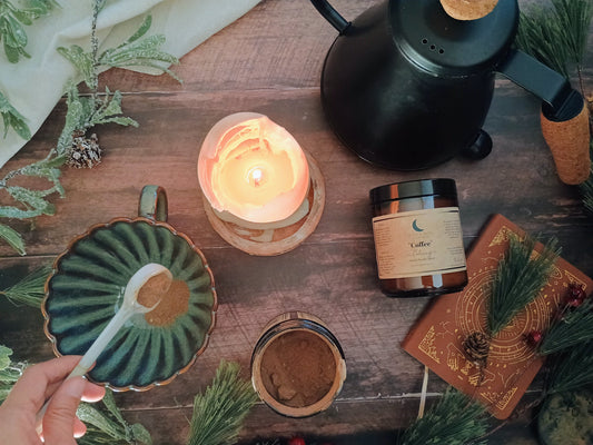 herbal alternative coffee being added to a mug with a lit candle, journal, and tea kettle