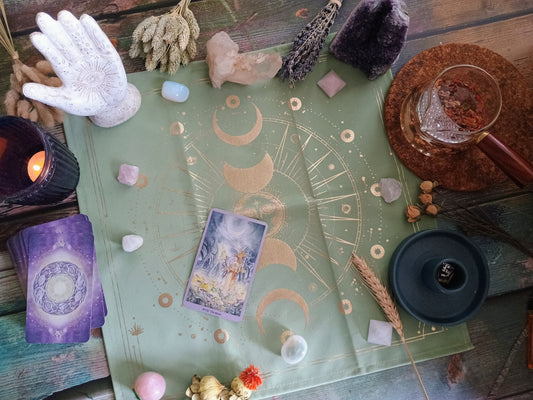 the moon tarot card, with crystals, a candle, florals, and palo santo