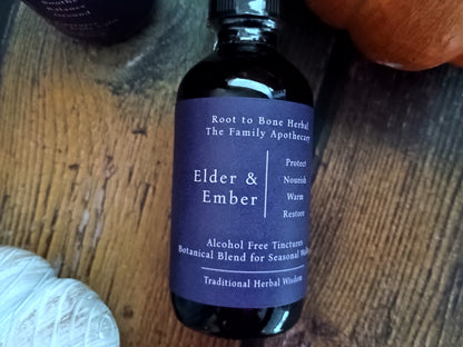 A dark amber glass bottle of Root to Bone Herbal 'Elder & Ember' tincture with a dark purple label, resting on a rustic wooden surface.