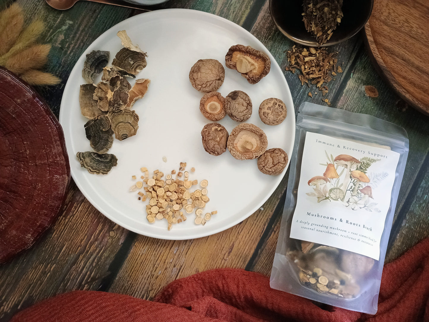 A styled flat-lay of a mushroom and krest bag next to its white plate of ingredients, including sliced dried mushrooms, chopped beige spores, and a whole mushroom, on a rustic wooden table.