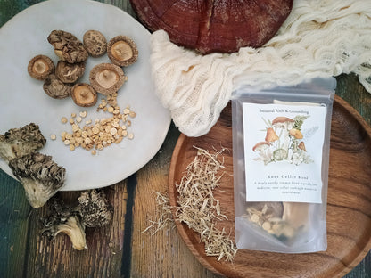 A styled flat-lay of a mushroom growing kit or spore print package labeled 'Root Cellar Blend' on a wooden tray, alongside sliced mushrooms, grain, dried herbs, a white plate, and a rustic wood slice on a dark wooden surface.