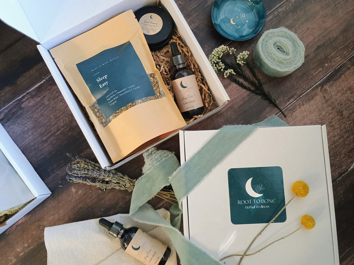 Gifting box with wellness products including a bottle, tea, and salve on a wooden surface.