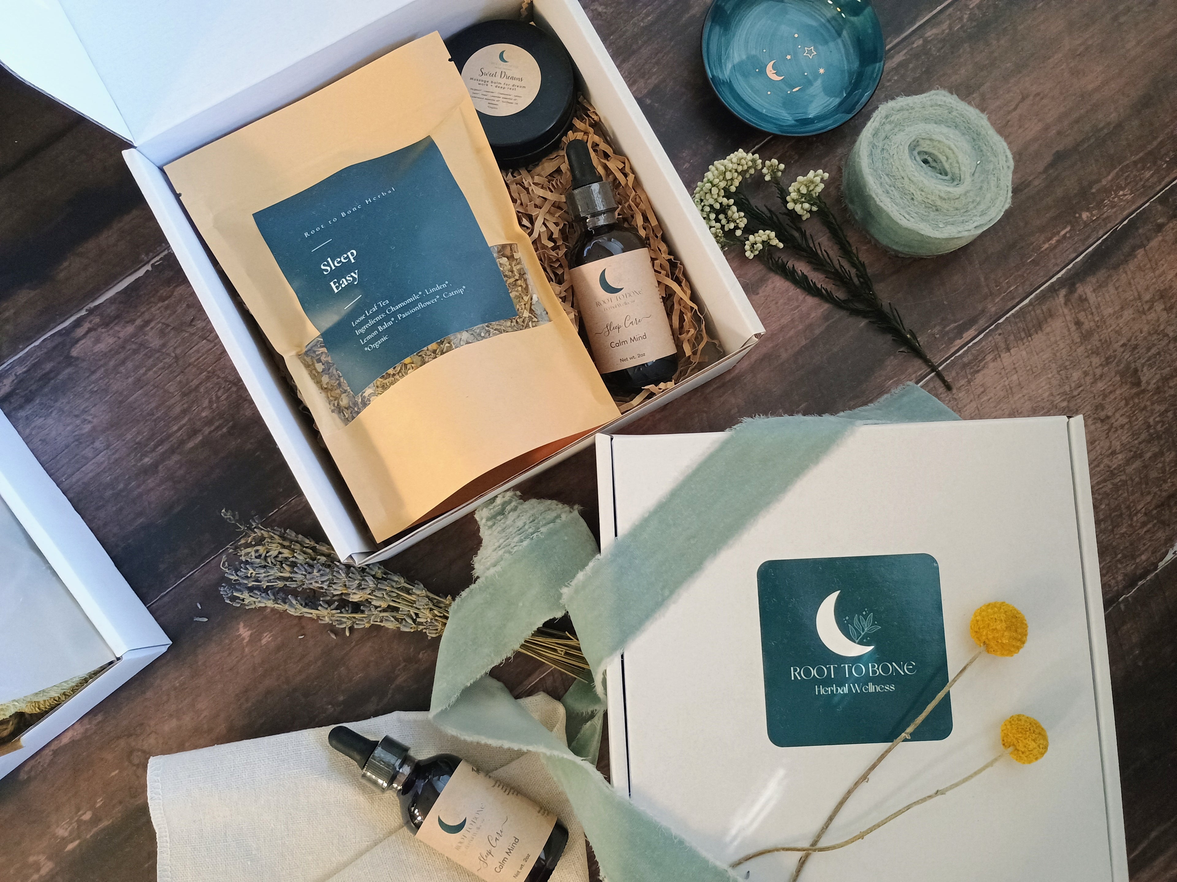 Gifting box with wellness products including a bottle, tea, and salve on a wooden surface.