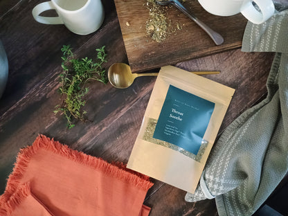 Tea package on a wooden surface with tea leaves and a spoon and thyme