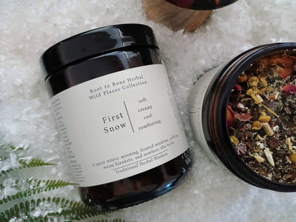 Two amber glass jars of First Snow Herbal Wild Places Collection herbal tea on a bed of white shavings, with one jar open to show the dried botanical blend inside.