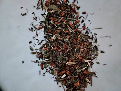 A small pile of loose dried herbal tea blend containing green, brown, and reddish-orange botanical pieces on a plain white surface.