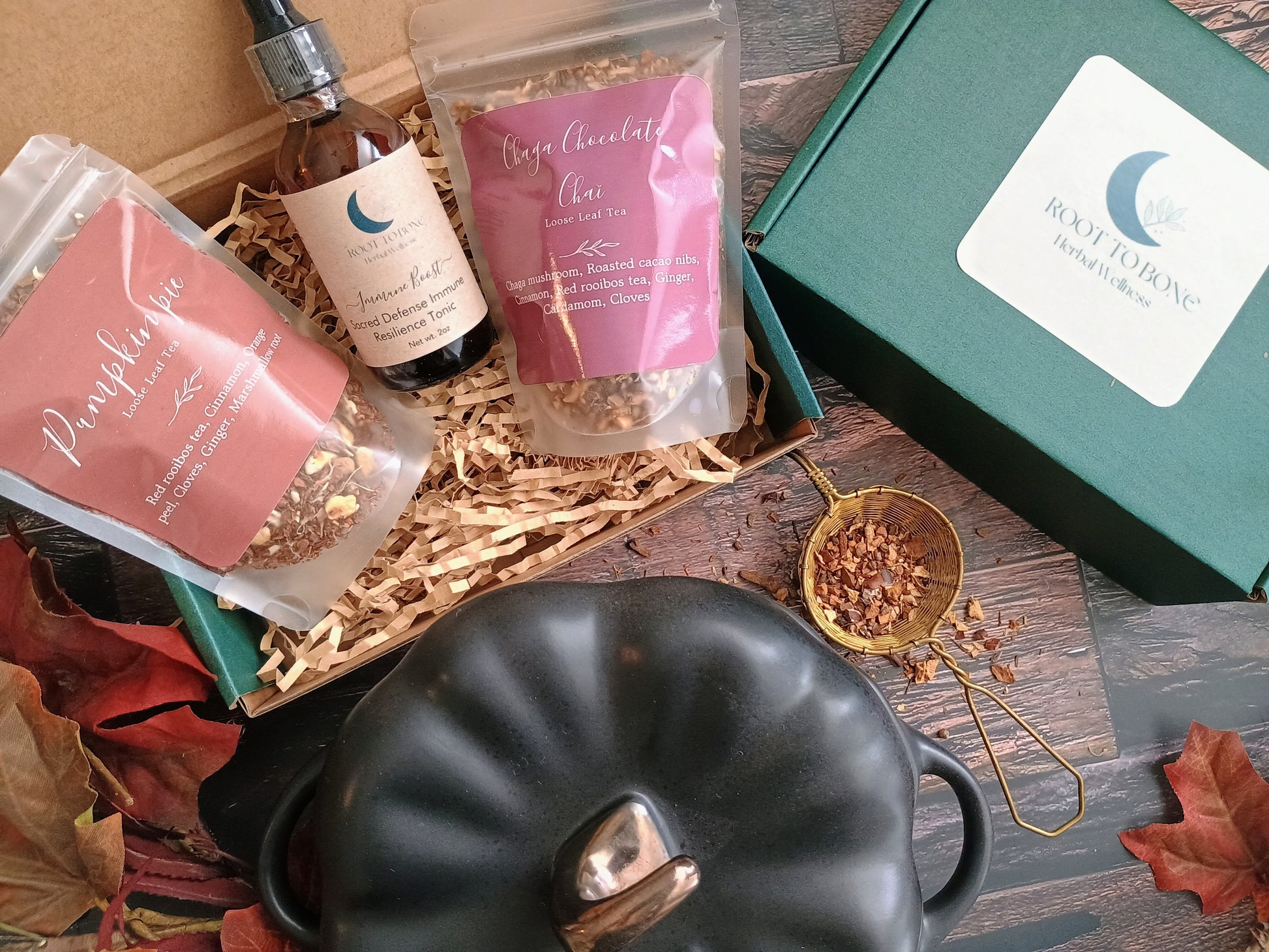 Gift set with tea, chocolate, and a pumpkin-shaped pot on a wooden surface.