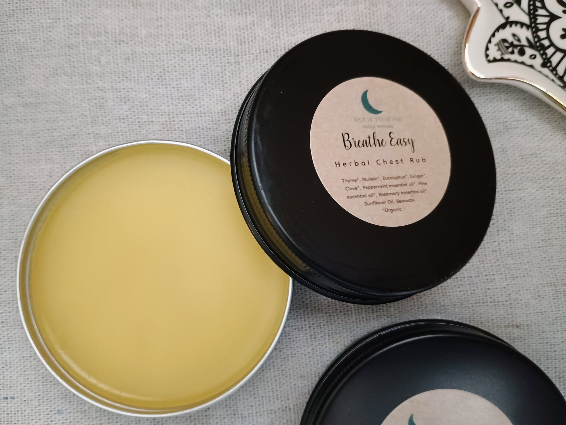 Open container of 'Breathe Easy' herbal chest rub with a black lid on a textured surface.