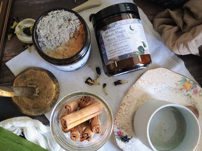 Spices and herbs on a wooden tray with a bowl of cinnamon sticks and a jar labeled 'Dreams Magic Moon Milk'.