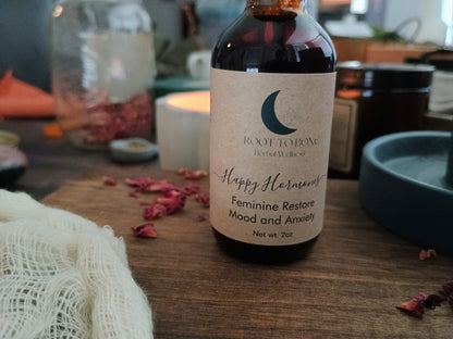 Bottle of 'Happy Hormones feminine restore' with a label on a wooden surface with dried flowers and candles.