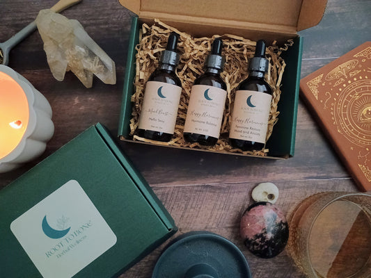 Three bottles of Root to bone Herbal Extracts in a gift box on a wooden surface with candles and stones.
