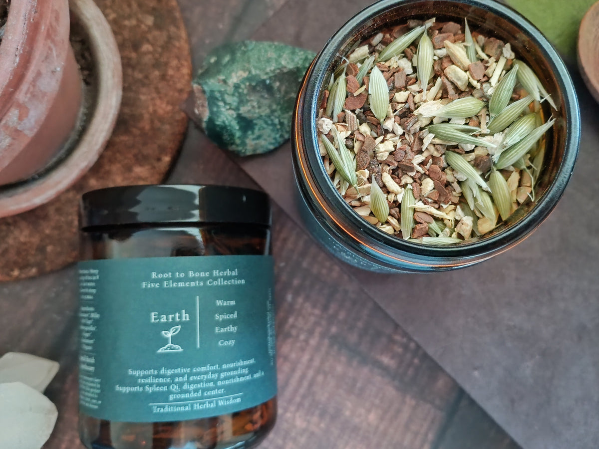 An amber glass jar labeled 'Root to Bone Herbal' from the 'Five Elements Collection' by Earth, shown next to an open jar displaying dried botanical ingredients like green cardamom pods and brown bark pieces.