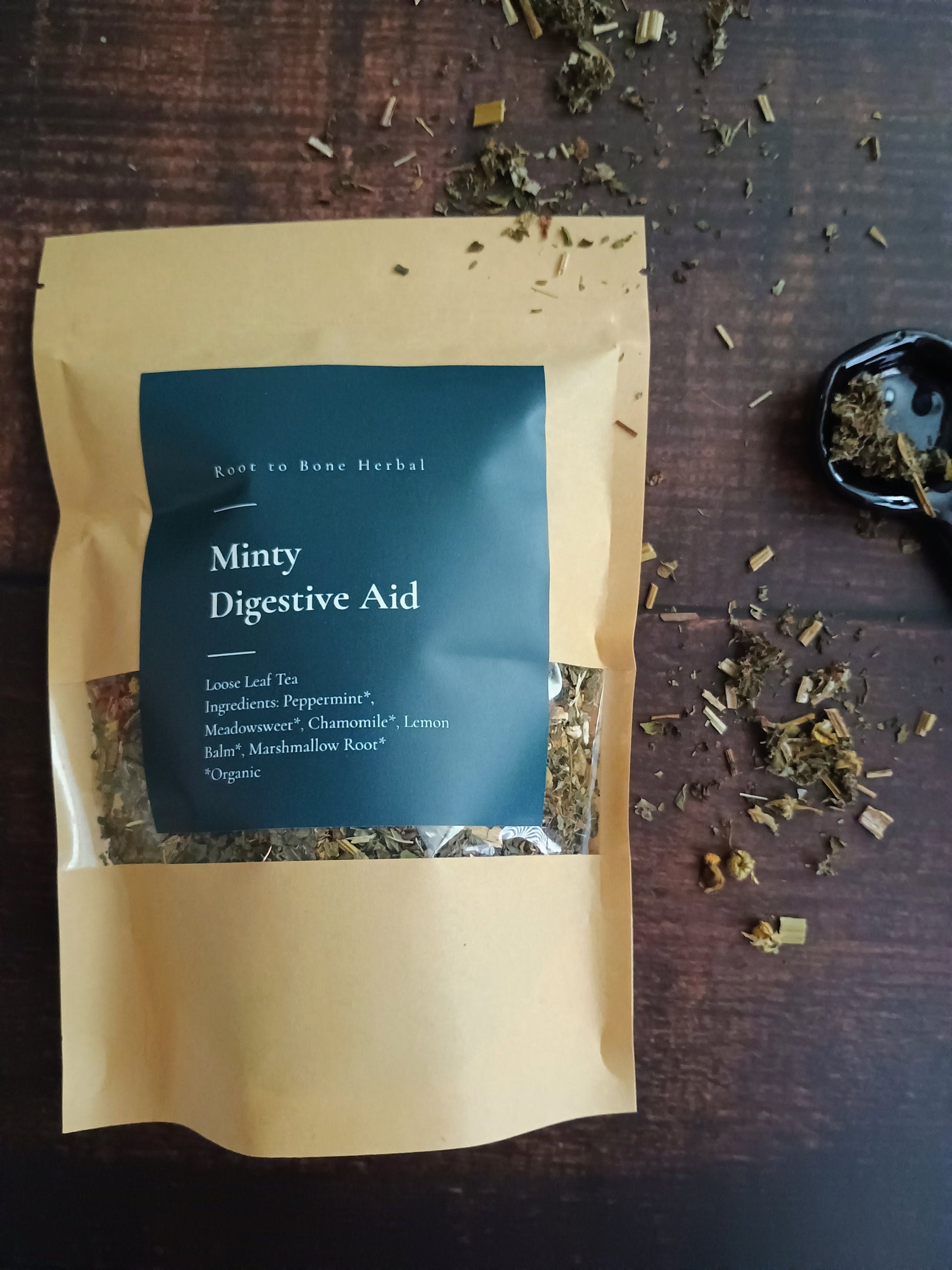 Tea package labeled 'Miny Digestive Aid' on a wooden surface with loose tea leaves.