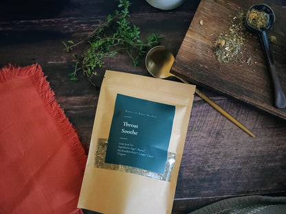Package of 'Throat Soothe' on a wooden surface with herbs and a spoon.