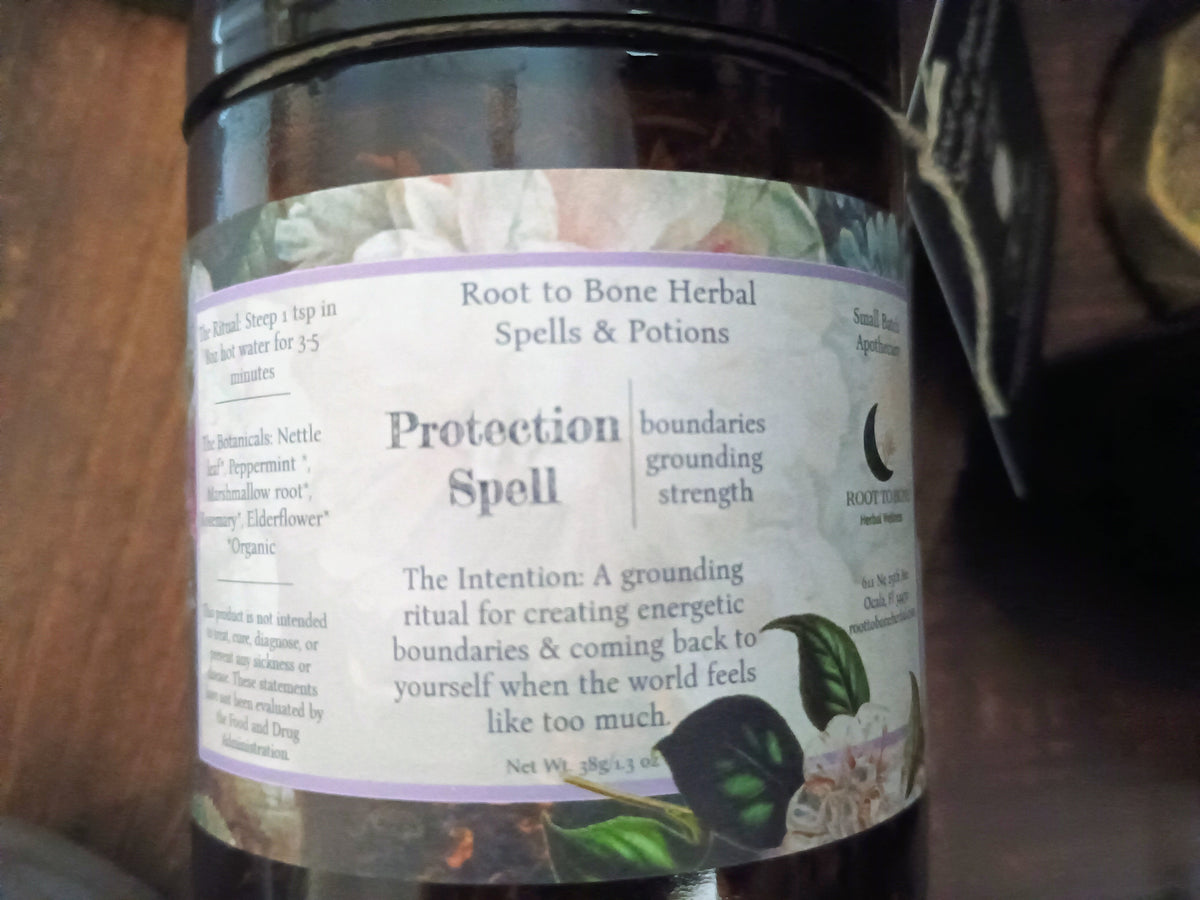 A dark glass jar of Root to Bone Herbal Spells & Potions Protection Spell, featuring a white label with purple text and botanical illustrations, set against a dark, rustic background.