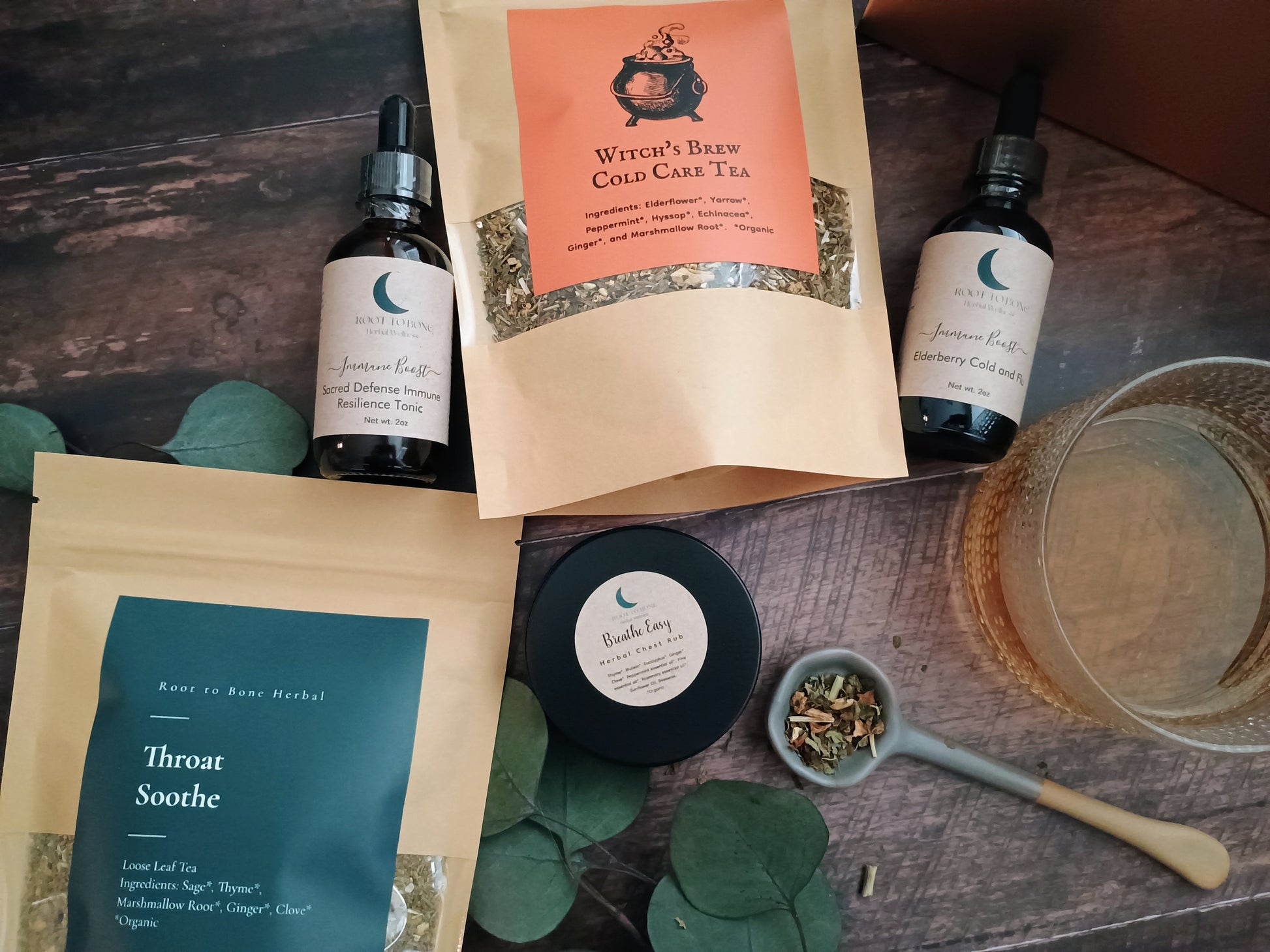 Herbal tea packaging, bottles, and a bowl on a wooden surface with green leaves.