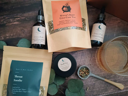 Herbal tea packaging, bottles, and a bowl on a wooden surface with green leaves.