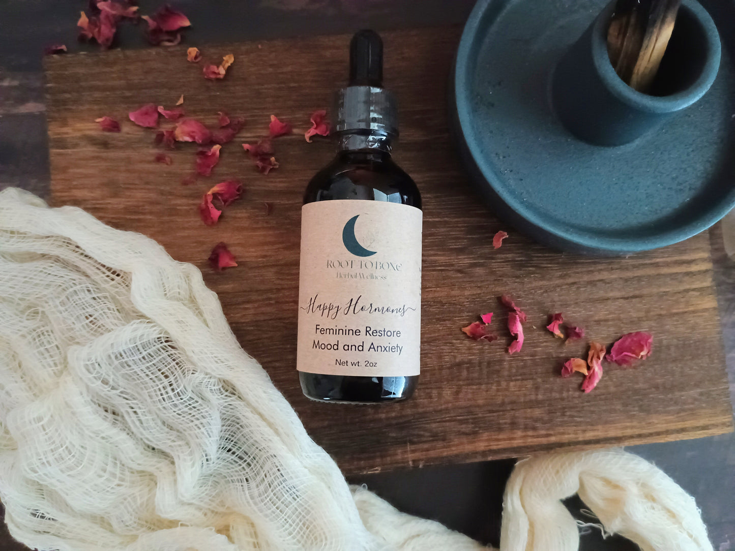 Bottle of 'Happy Hormones feminine restore' on a wooden surface with dried flowers and a blue candle holder.