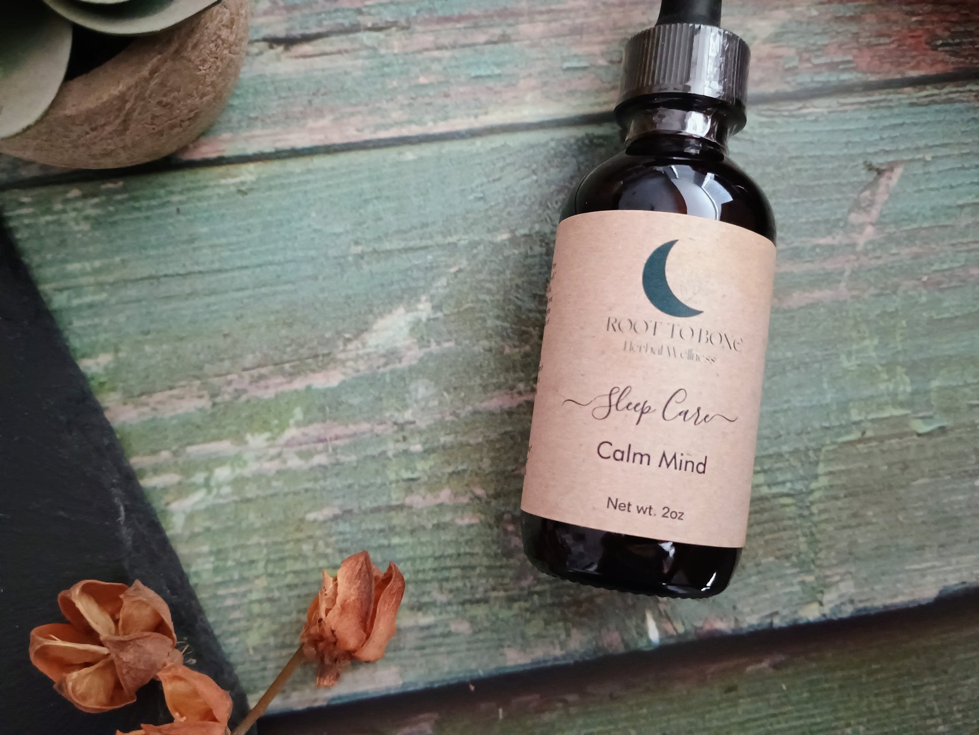 Bottle of 'Calm Mind' sleep care product on a wooden surface with dried flowers.