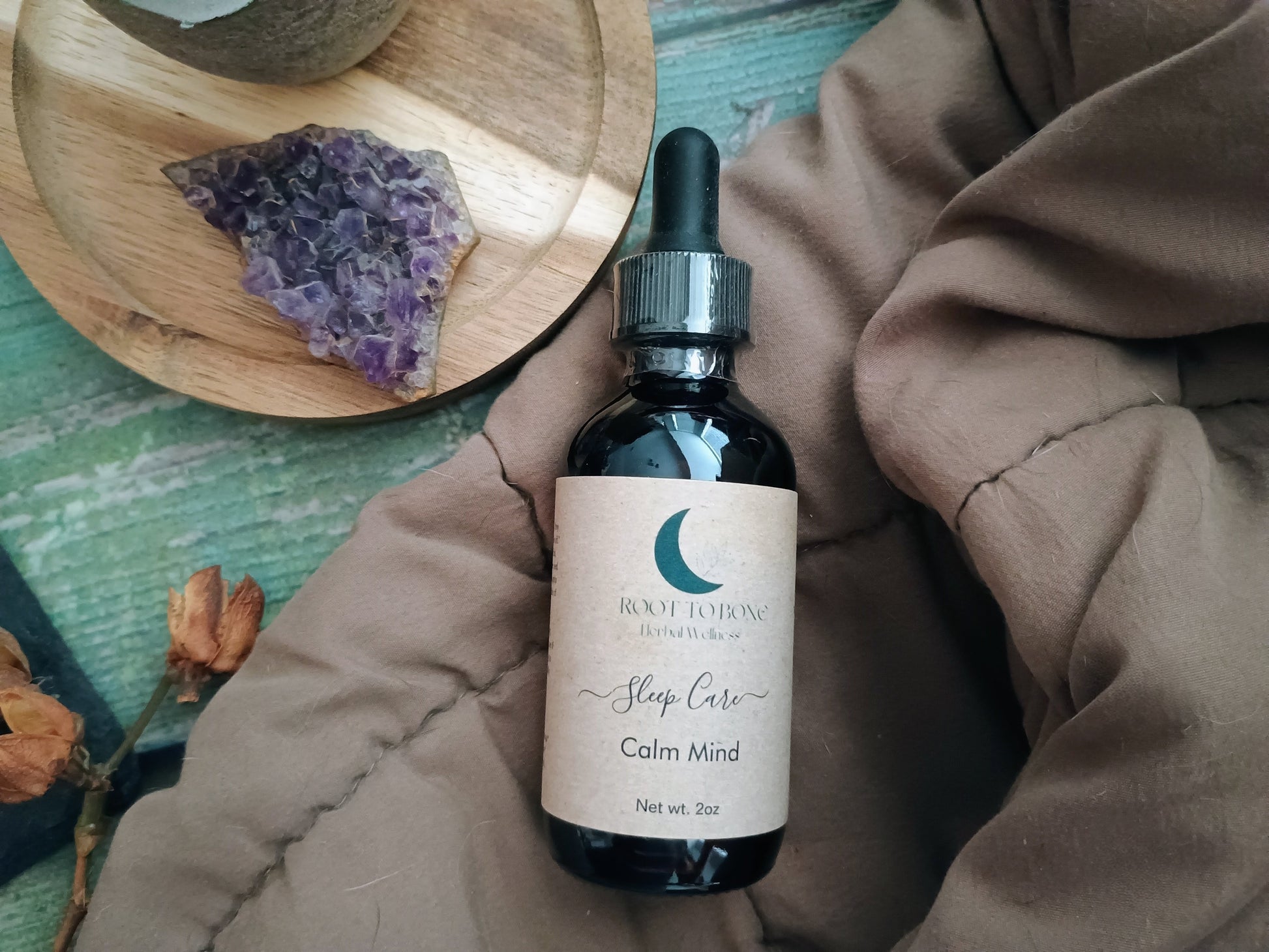 Bottle of 'Calm Mind' sleep care product on a textured surface with a wooden plate and crystals in the background.