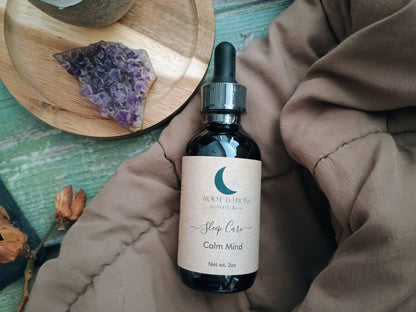 Bottle of 'Calm Mind' sleep care product on a textured surface with a wooden plate and crystals in the background.