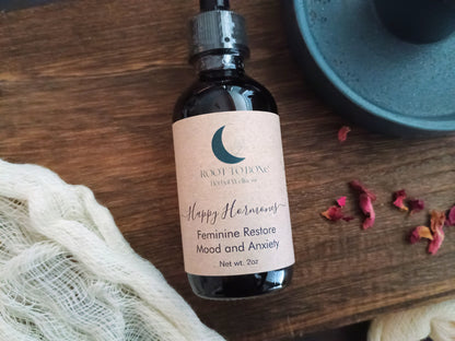 Bottle of 'Happy Hormones Feminine Restore Mood and Anxiety' on a wooden surface with a blue container and dried flowers.
