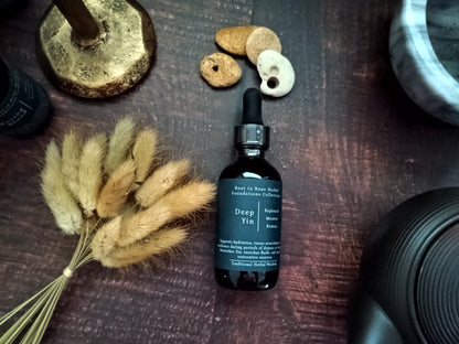 A dark amber glass dropper bottle labeled 'Deep Yin' by Root to Bone Herbals, styled on a dark wooden surface with dried bunny tail grass, small stones, and a brass candle holder.