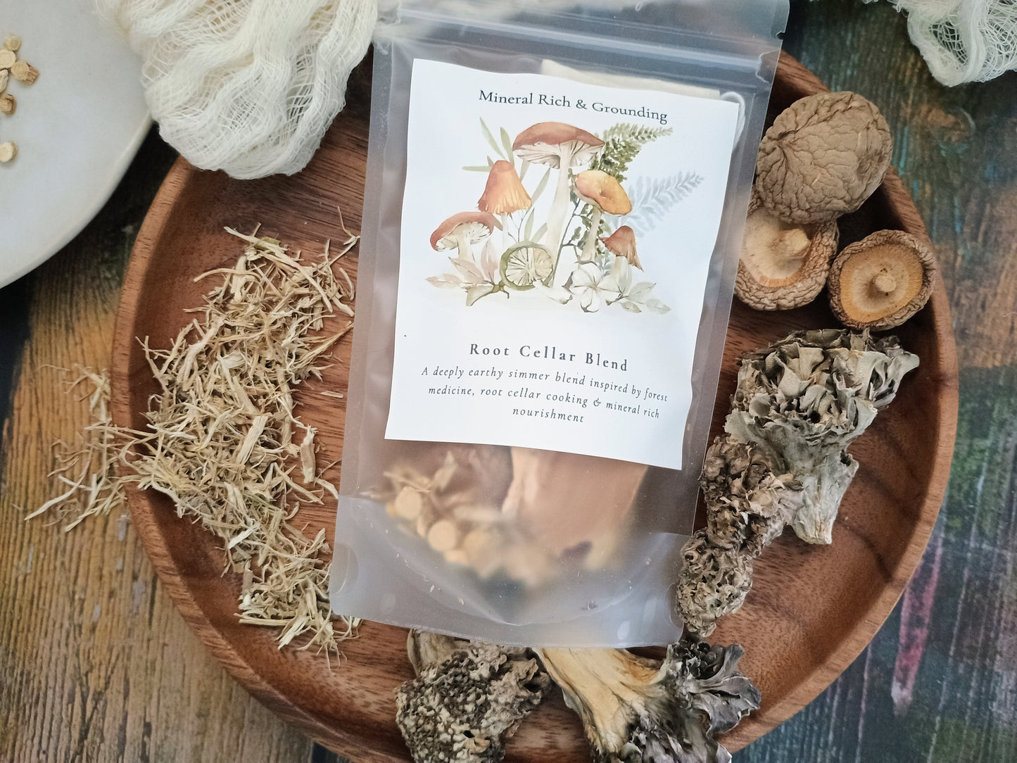 A clear stand-up pouch labeled 'Koot Cellar Blend' with mushroom illustrations, placed on a wooden tray surrounded by dried mushrooms and herbs.