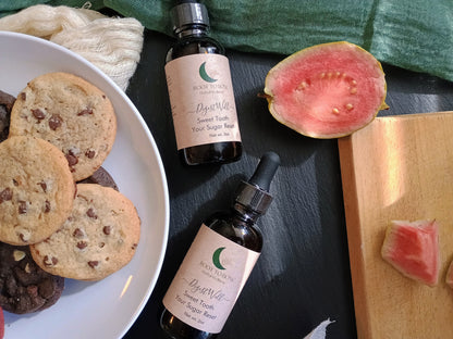 Two bottles of 'Root to Bone herbal' tincture on a dark surface with cookies and a watermelon slice.