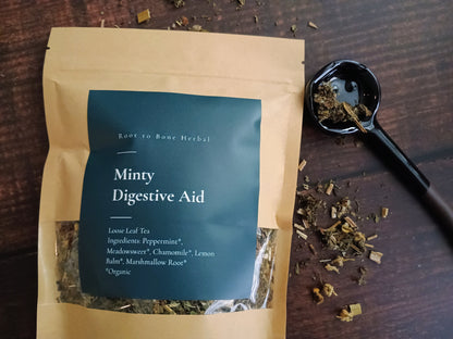 Tea package labeled 'Minty Digestive Aid' on a wooden surface with tea leaves.