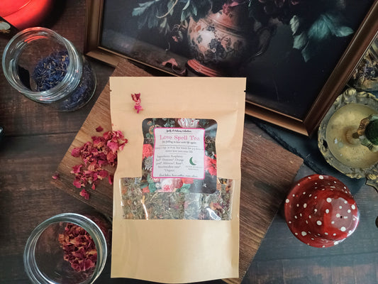 Tea package on a wooden surface with dried flowers and a framed picture in the background
